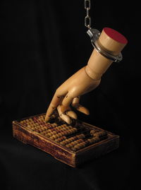 Close-up of wooden hand with handcuffs and abacus over black background