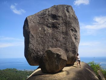 Rear view of sculpture on rock formation in sea against sky