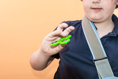 Midsection of boy holding fidget spinner against yellow background