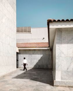 Full length of man walking by building in city during sunny day