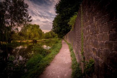 Footpath by river amidst trees against sky