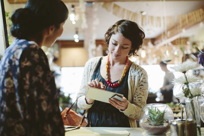 Owner looking at customer making card payment at counter in plant shop