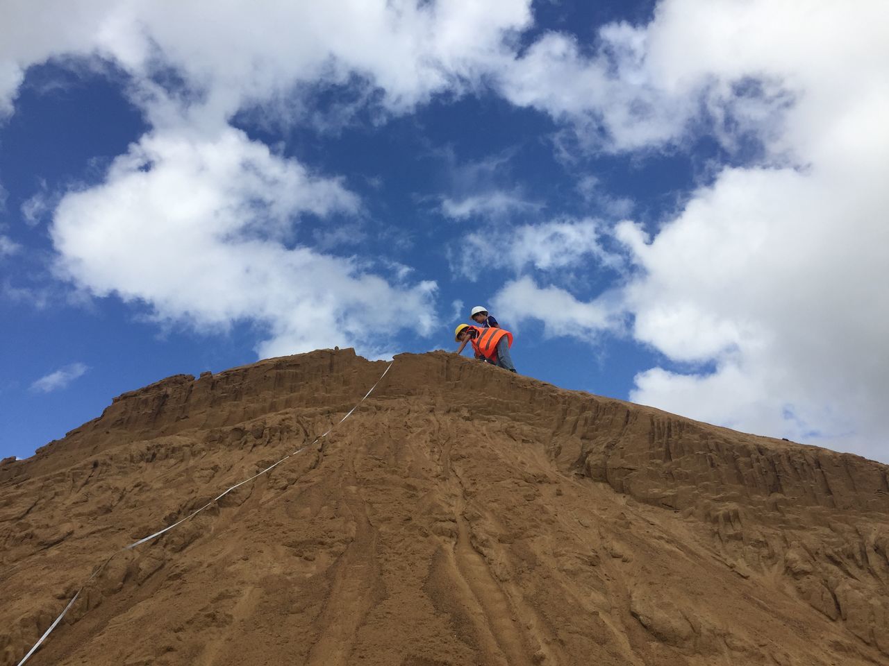 low angle view, sky, leisure activity, lifestyles, cloud - sky, full length, cloud, men, adventure, cloudy, day, extreme sports, outdoors, freedom, casual clothing, standing, risk, climbing