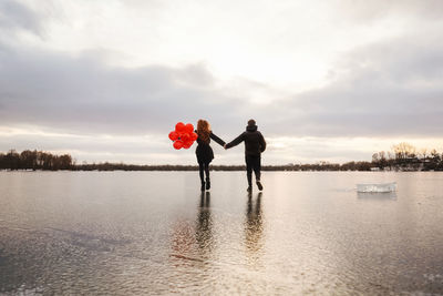 Rear view of couple holding hand walking on frozen lake against sky