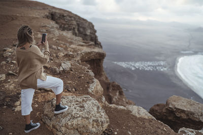 Rear view of woman standing on rock by sea