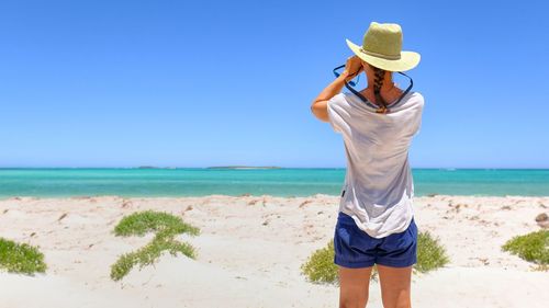 Rear view of woman standing on beach against clear sky