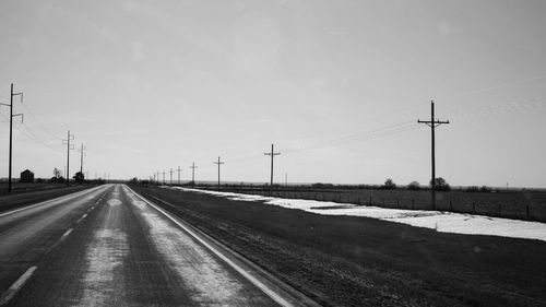 Road by electricity pylon against clear sky