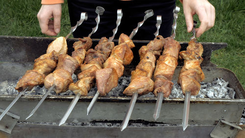 Midsection of person preparing meat on barbecue at lawn