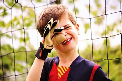 Close-up of playful boy making face against netting on soccer field