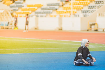 Full length of female athlete sitting at stadium