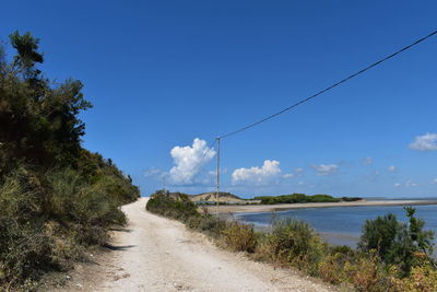 Scenic view of road amidst trees against blue sky