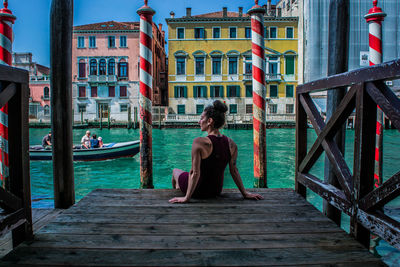 Rear view of woman sitting on pier over canal