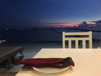 Deck chairs on shore against sky during sunset