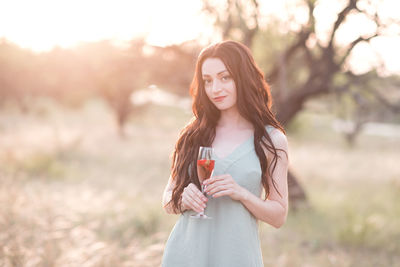 Beautiful smiling woman holding glass of wine with strawberry outdoors over nature background. 