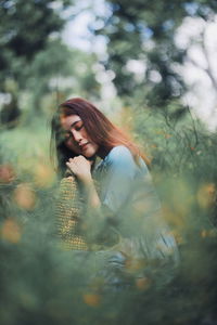 Side view of young woman crouching amidst plants on field