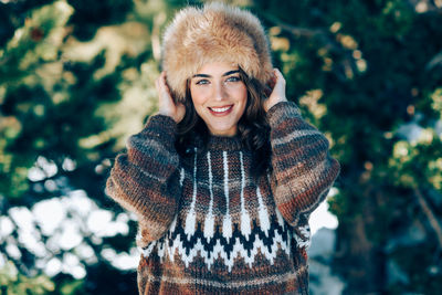 Portrait of smiling young woman standing by tree during winter