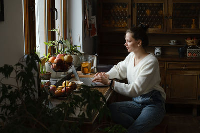 Young freelancer working on laptop at home. woman using computer on the kitchen for work. distant