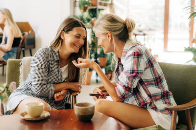 Two stylish female girlfriends are talking while sitting in a cafe.