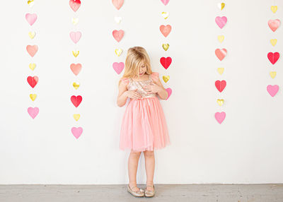 Young blond girl in fancy dress in front of hearts indoors