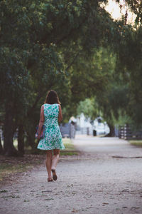 Rear view of woman walking on road amidst trees