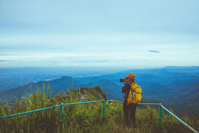 Rear view of woman photographing on mountain against sky