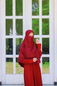 Woman in hijab standing against window