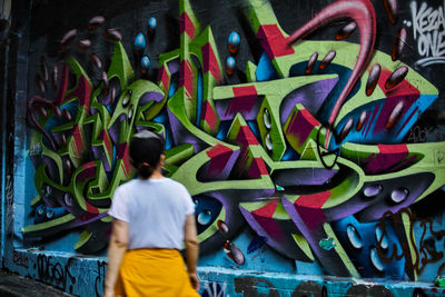 Rear view of boy standing against graffiti wall