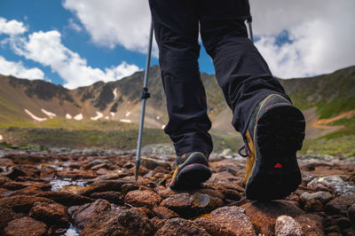 Hiking boots close-up on mountain rocks by the lake with trekking poles, view from below