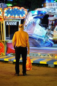 Rear view of man standing on illuminated street at night