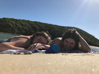 Portrait of smiling friends lying on beach against clear sky during sunny day