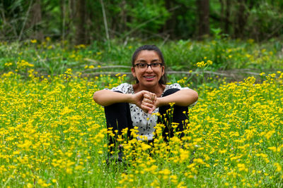 Portrait of smiling young woman with yellow flowers on field