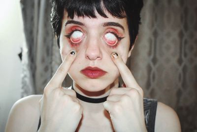 Close-up of young woman pulling her eyes at home