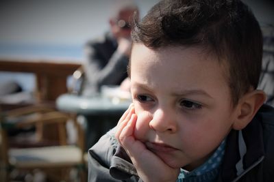 Close-up of cute boy with hand on chin looking away