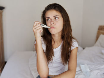 Portrait of beautiful young woman sitting on bed at home