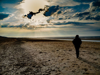 Rear view of man standing on beach against sky during sunset