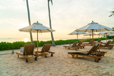 Empty chairs and tables at beach against sky