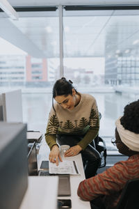 Businesswoman showing document while discussing strategy with female colleague at desk in office