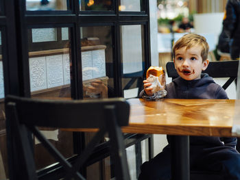 Toddler boy in casual clothes eating a chocolate bun in a food court there is a chocolate on face