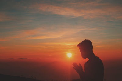 Side view of silhouette man standing against orange sky