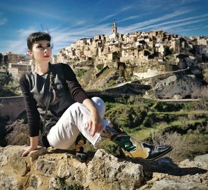 Young woman sitting on rock against sky