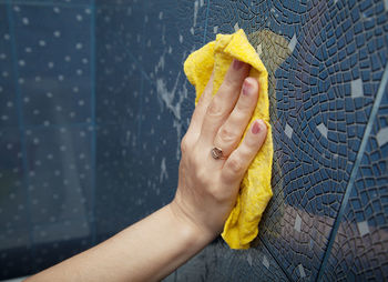 Cropped hand of woman cleaning tiled wall at home