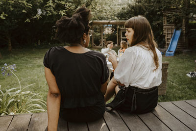 Rear view of young woman talking to female friend while sitting in backyard