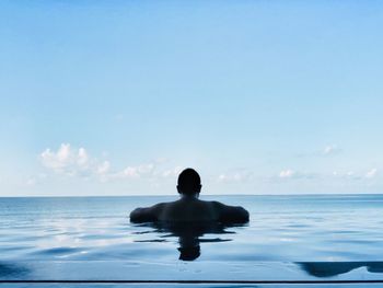 Rear view of shirtless man swimming in infinity pool against sea