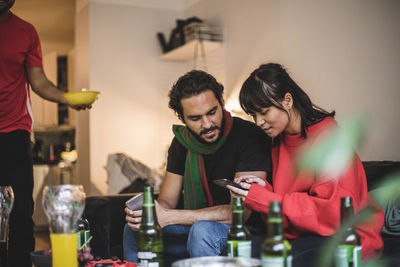 Male and female friends using smart phone while watching match at home