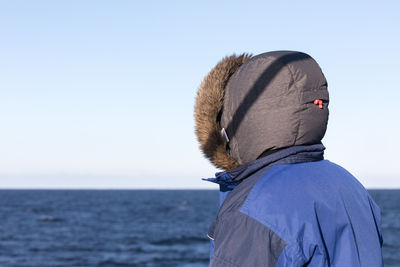 Rear view of man standing by sea against clear sky