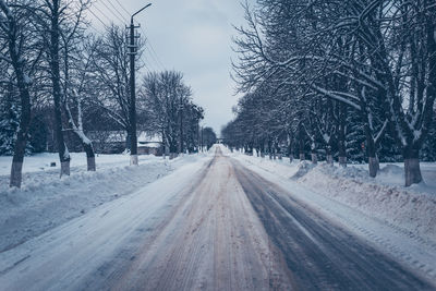 Snow covered road amidst trees against sky