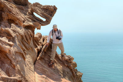 Man on rock formation against sky