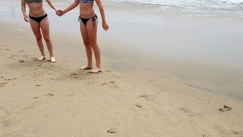 Low section of young woman in bikini standing on sandy beach