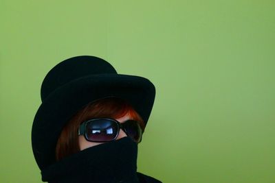 Close-up of woman wearing hat and sunglasses against green background