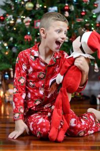 Cheerful boy looking at stuffed toy while sitting by christmas tree